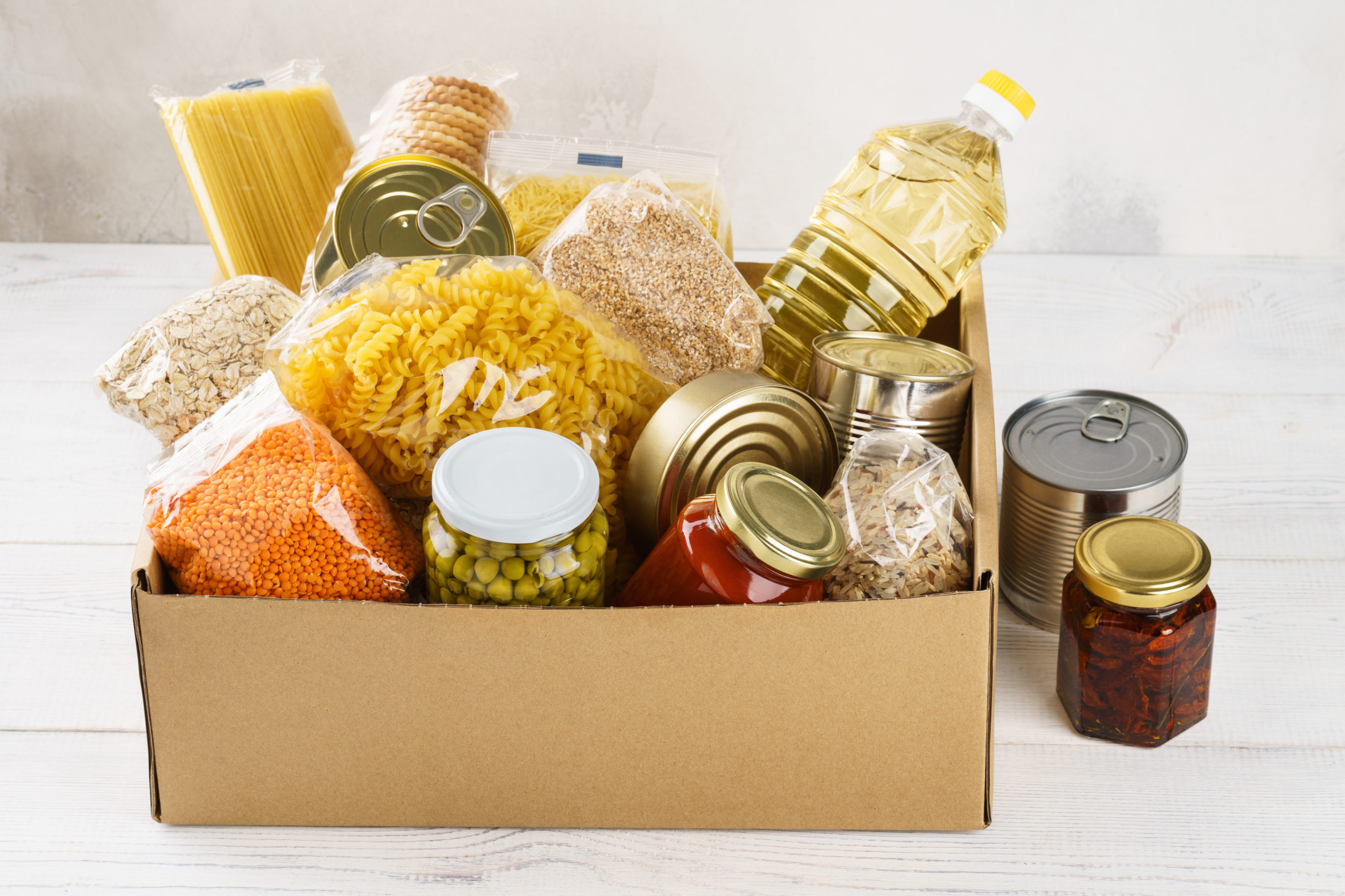 Various canned food, pasta and cereals in a cardboard box. Food donations or food delivery concept.